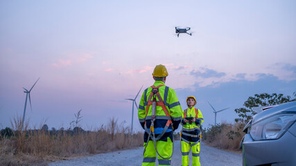 Engineer surveyor team under used drone camera for operator inspecting and survey construction site with windmill turbine farm background.