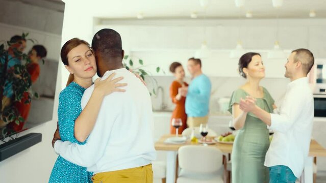 Smiling attractive woman in russet dress enjoying slow dance with black man at relaxed friendly home gathering. High quality 4k footage