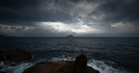 Cloudy day on the sea, sunlights shines between cloud, and a little island in the distances, in...