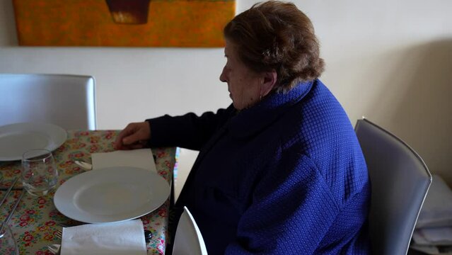 Grandmother settling in at the table, patiently awaiting family mealtime gathering. Panning