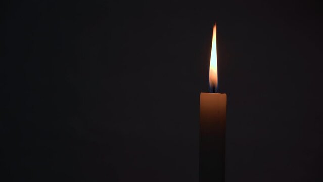 Brightly burning wax candle in the dark on a black background. Place for text. Concept of loss, grief, sorrow. Symbol of suffering and death. High quality 4k footage