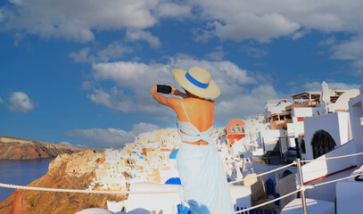 Young tourist woman backpack using smartphone take picture at View of blue church dome in Oia village,Santorini,Greece