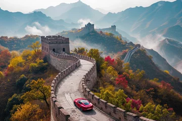 Gordijnen A red car is seen driving down a road that runs adjacent to a majestic mountain, A sports car driving along the Great Wall of China, AI Generated © Iftikhar alam