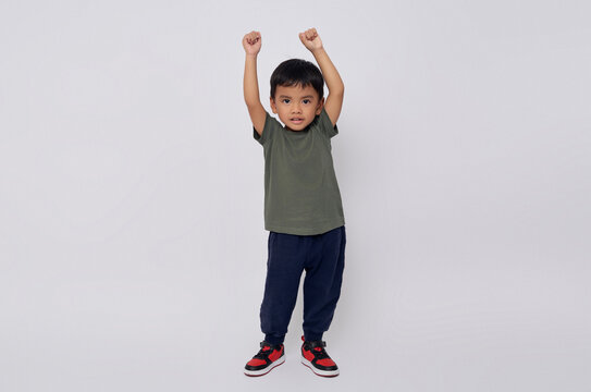 Full body little small smiling happy Asian boy 2-3 years old wearing green t-shirt standing confident while doing winner gesture isolated on white background