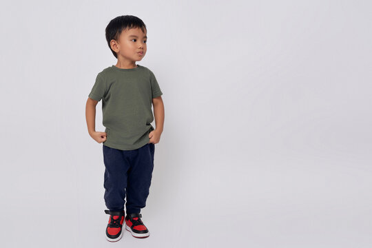 Full body little small smiling happy Asian boy 2-3 years old wearing a green t-shirt standing confident while looking at copy space isolated on white background
