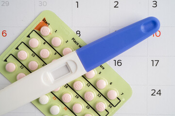 Pregnancy test and birth control pills on calendar, contraception health and medicine.
