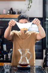 young barista lifts coffee filter into drip coffee maker
