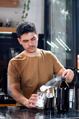 young barista pours ice into glass with small scoop