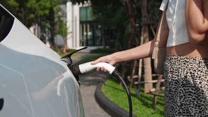 Young woman recharge EV electric car battery at residential area EV charging station in smart home...