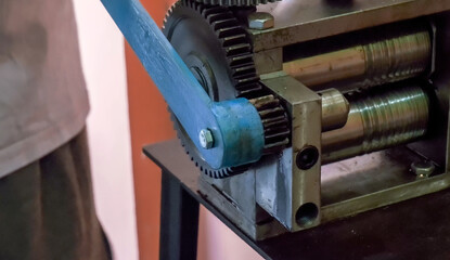 Goldsmith using a press to roll silver ring blank. Close up. Jewelry handicraft