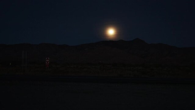 Time lapse video of moon rising over mountain range with vehicles driving by in Nevada.