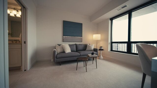 push in shot of a cozy den area in a home with a grey couch and large windows letting in natural light