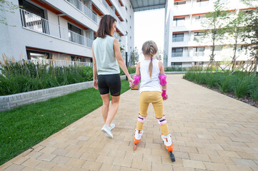 Mother helps daughter learn to roller skate. 