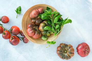 Pink ribbed tomatoes and basil in a bowl on a blue background. Harvest of tomatoes. Seasonal vegetables.