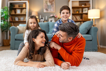 Happy parents and their small kids talking while lying on carpet at home.