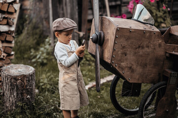 A young aviator boy near a homemade airplane in a natural landscape to fix a propeller with a...
