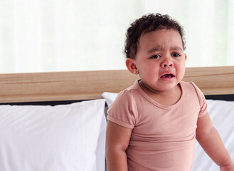 Portrait of sad dark-skinned child girl crying in the bedroom against white wall background at home.