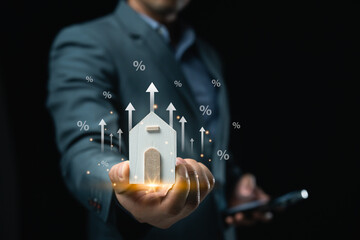 Businessman holding a phone and a house with virtual house symbol. The house Property interest is...