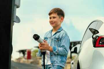 Little boy recharging eco-friendly electric car from EV charging station. EV car road trip travel...