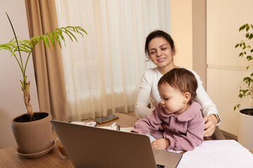 Cheerful pretty businesswoman working at home with her little child girl