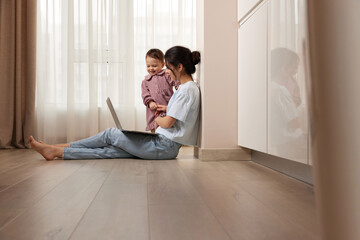 beautiful casual woman sitting on the floor and working on laptop with her little child girl at home