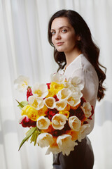 Beautiful woman in the white shirt with spring flowers tulips in hands. Women's Day