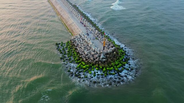 Sea breakwater with tetrapod concrete pillars covered with green moss with ocean waves, aerial footage from drone.