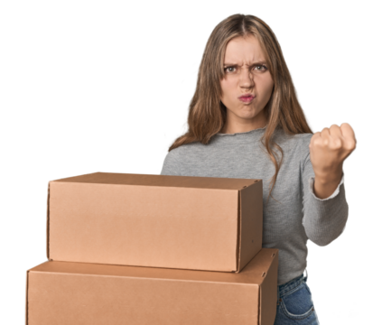 Blonde woman with cardboard boxes moving on studio backdrop showing fist to camera, aggressive facial expression.