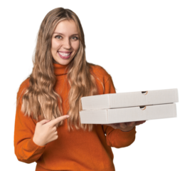 Blonde woman holding pizza boxes in studio smiling and pointing aside, showing something at blank space.