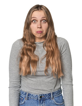 Studio portrait of a blonde Caucasian woman shrugs shoulders and open eyes confused.