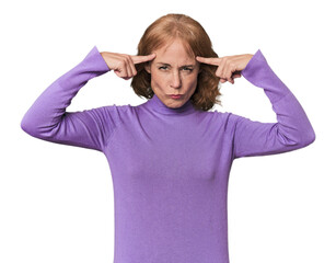 Redhead mid-aged Caucasian woman in studio focused on a task, keeping forefingers pointing head.