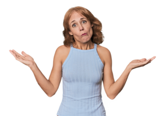Redhead mid-aged Caucasian woman in studio doubting and shrugging shoulders in questioning gesture.