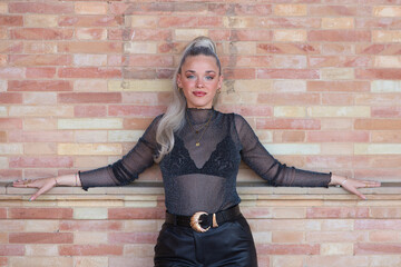 Pretty young blonde woman with a ponytail in her hair leaning with her arms outstretched on the brick wall in the plaza de espana in seville. The girl is a model and poses for photos.