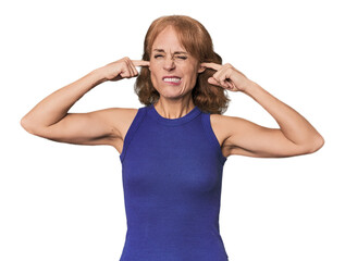 Redhead mid-aged Caucasian woman in studio covering ears with fingers, stressed and desperate by a...