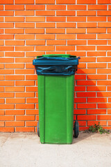 Green plastic garbage can against orange brick wall