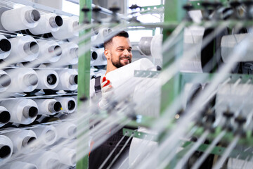 Textile factory worker changing thread spool on industrial knitting machine.