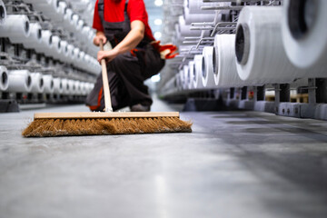Unrecognizable worker cleaning floor with broom. Keeping factory neat and clean.