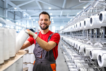 Portrait of worker holding thread spool inside textile factory. In background industrial knitting machine.