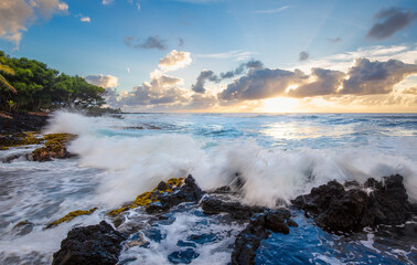 Sunset over the sea, waves crashing on the rocks, palm trees on the beach in Hawaii. Big Island, United States of America.