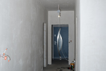 Prace wykończeniowe w nowym domu, zagruntowane ściany w korytarzu, wystająca elektryka w trakcie remontu