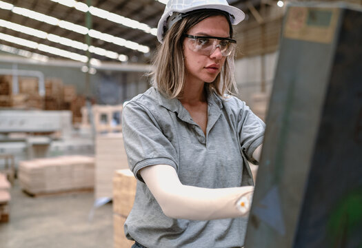 Confident female worker standing in lumber warehouse of hardwood furniture factory inspecting production machine. Serious technician woman, engineer busy working with tool in woodwork manufacturing.