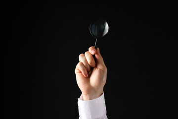 A businessman's hand holds a magnifying glass on a black background