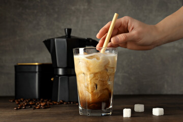 Glass with iced coffee drink and straw, coffee maker, coffee bean, hand and sugar on gray background