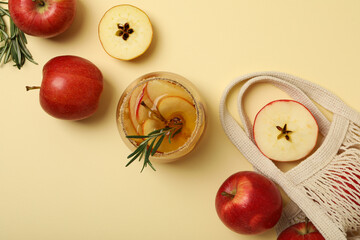 Glass of apple cider, rosemary branch and apples in bag on beige background, top view