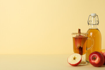 Glass cup and bottle with apple cider and red apples on beige background, space for text
