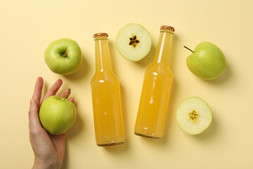 Glass bottles with cider, green apples and hand on beige background, top view