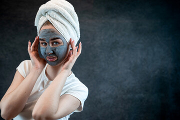 Portrait of attractive young woman apply clay mud mask on her face isolated on black