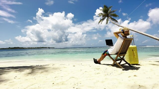Nomad digital young man with the laptop and running remotely with bright scenic view near poolside on the beach in summer time