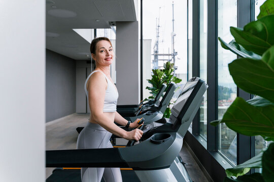 Smiling woman doing cardio training on treadmill at gym