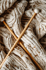 A close up of brown wooden knitting needles on a pile of grey and beige knitted fabric. The intricate pattern showcases the art of textile using woolen materials.  - 761249499
